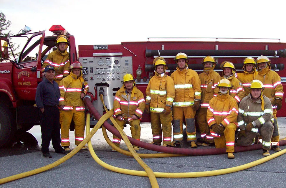 Firefighters in gear posing in front of a fire engine with hoses